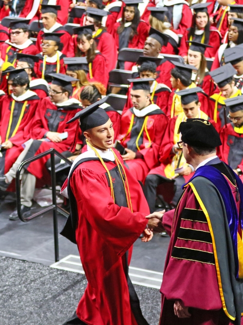 SAS grad crossing stage and shaking hands with Dean with fellow graduates watch.